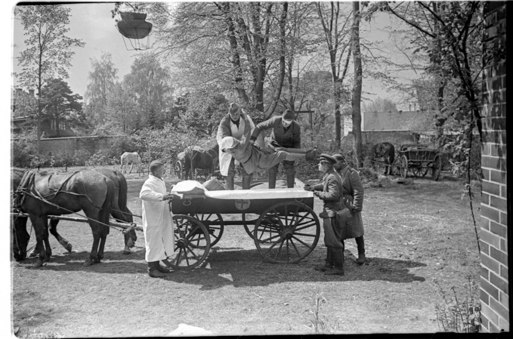 Медики укладывают раненого на санитарную конную повозку с обозначением Красного Креста